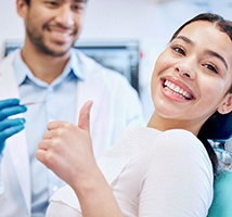 Woman smiling while giving thumbs up next to dentist