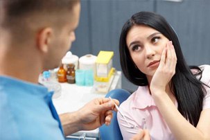 Woman in dental chair holding cheek