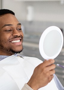 Man smiling at reflection in handheld mirror