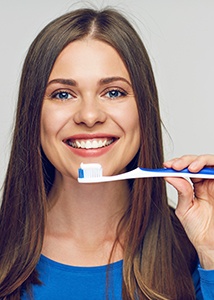 a patient smiling while brushing her teeth