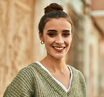 A young woman wearing a green sweater is smiling after receiving her customized dental implant in Jonesboro