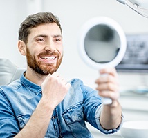 A man with a beard looking at his new smile in the mirror in Jonesboro