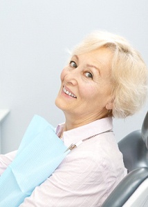 Senior dental patient holding mirror, admiring her implant-retained dentures