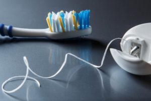 Floss container sitting beside a toothbrush on a dark surface 