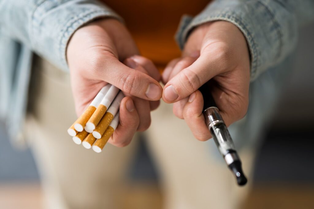 A person holding an e-cigarette and traditional paper cigarettes